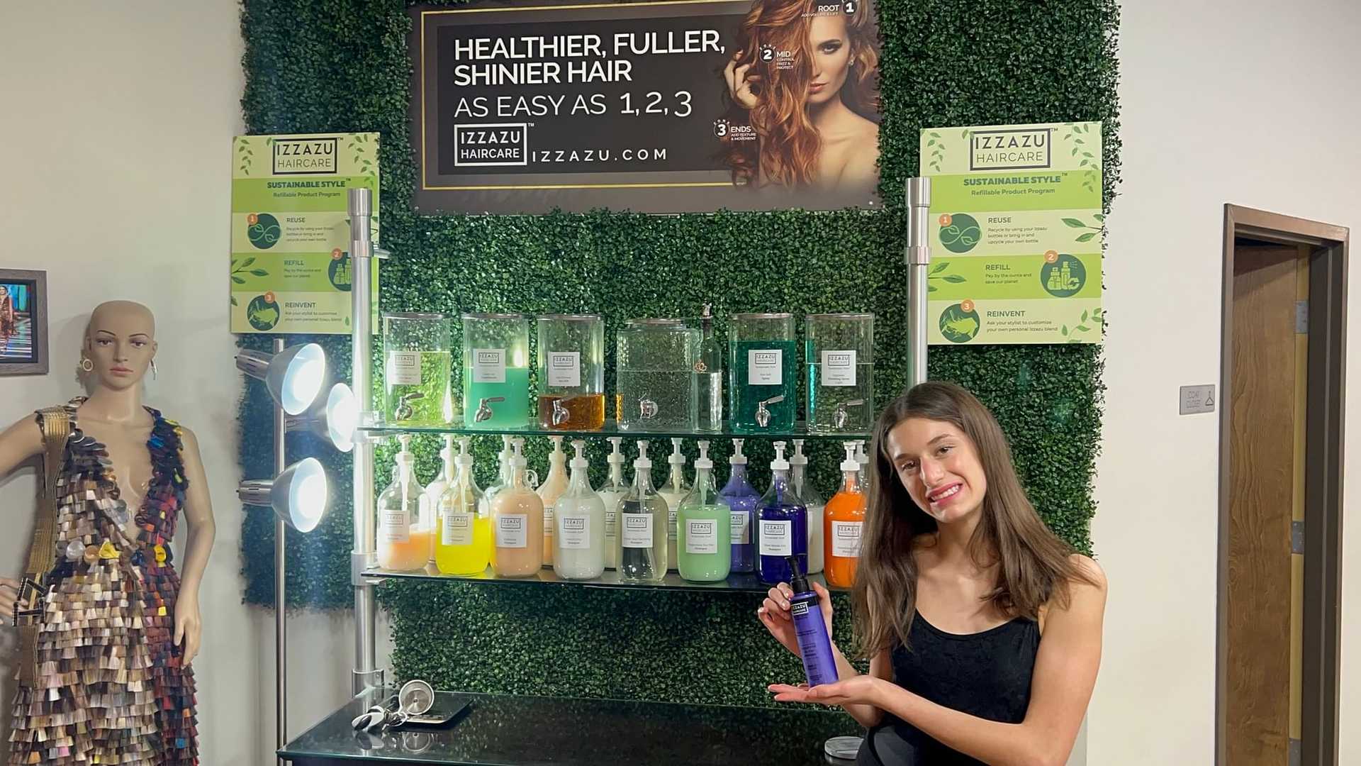 Woman holding hair product in front of store display with hair care products and promotional signage.